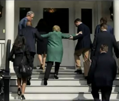 Hillary Clinton requires help from two men in orderto climb up a short set of steps